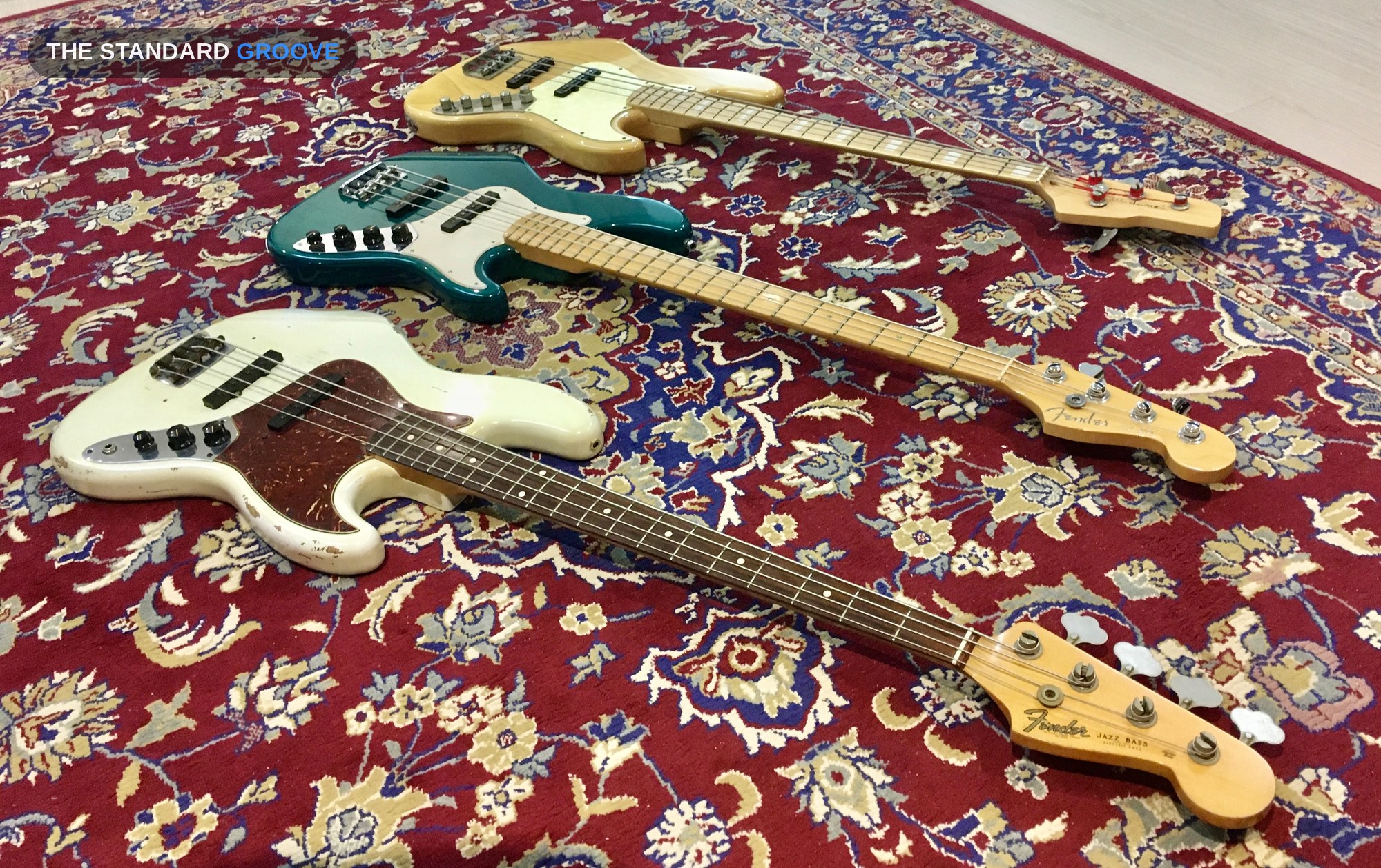 카펫 위에 나란히 놓인 Dame Jazz Special, Fender American Deluxe Jazz Bass Z2, Fender Jazz '64 Custom Shop Relic